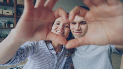 Portrait of cheerful couple making heart with their hands, looking at camera and smiling. Romantic relationship, happy married life and honeymoon concept. - Powered by Adobe