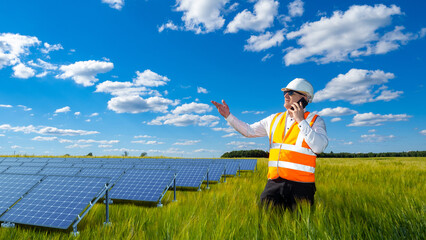 Sun power plant engineer. Man with phone In front solar panels. Farm with solar panels. Man dressed...