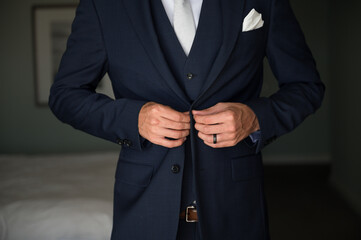 Groom getting ready for wedding buttoning navy suit jacket  close crop no face