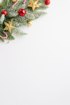 Christmas concept. Top view vertical photo of pine branch in frost decorated with red baubles gold star ornaments and candy canes on isolated white background with copyspace
