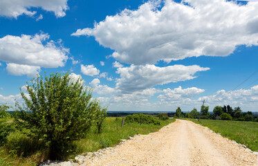 Fototapeta na wymiar Road through the field stretching into the blue sky