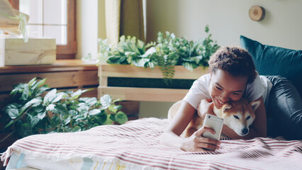 Joyful dog owner is taking selfie with cute friendly pet lying on bed together holding smartphone posing and hugging animal. Friendship between people and puppies concept.