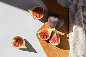 Top view of ripe juicy figs cut in slices on wooden cutting board. Trendy contrast light, white...