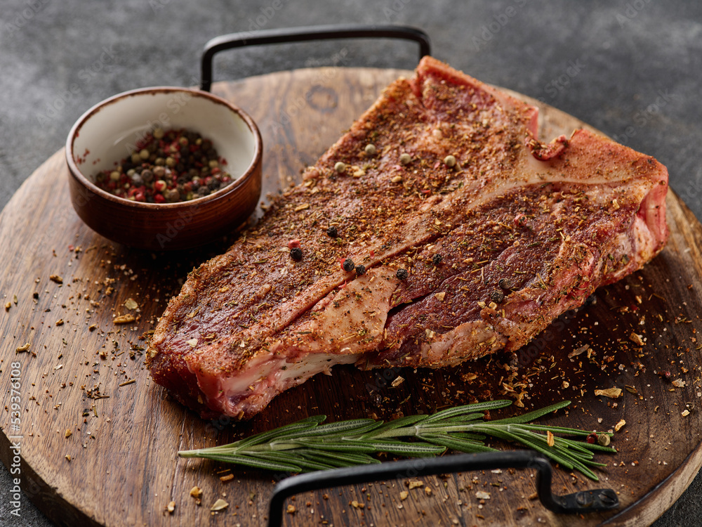 Wall mural raw fresh meat t-bone steak, seasoning on chopping cutting wooden board on grey background.