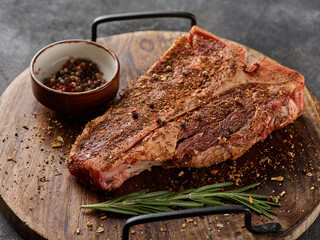 Raw fresh meat T-bone steak, seasoning on chopping cutting wooden board on grey background.