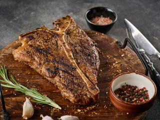 Grilled T-Bone Steak with salt and pepper  on cutting board on dark grey background. Roasted T-Bone beef steak.