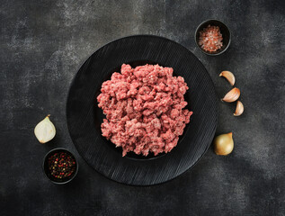 Fresh pork minced meat with salt, pepper and garlic, onion on grey background. Raw minced meat on...