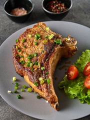 Grilled pork chop on grey plate sprinkled with green onions with salad and cherry tomatoes, close-up