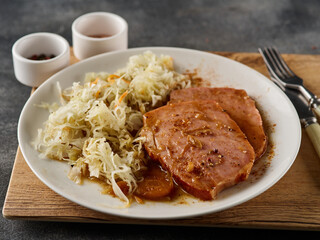 Backed Kasseler pork steak with sauerkraut. Smoked pork lion. Sliced smoked pork chop on wooden board