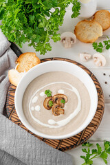 Mushroom cream soup with cream, croutons and herbs on a white wooden background. Delicious comfort food.