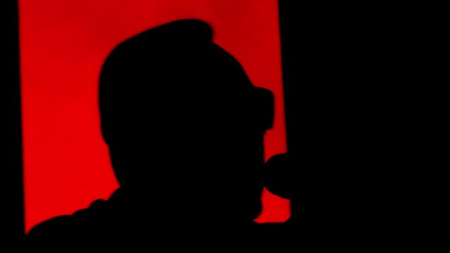 Male singer artist sings into a microphone on stage. Black silhouette of an artist on a red stage background, acoustic