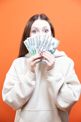 Winsome Surprised Cheerful Young Caucasian Girl Holding Money Currency Banknotes Isolated Over Orange Yellow Background