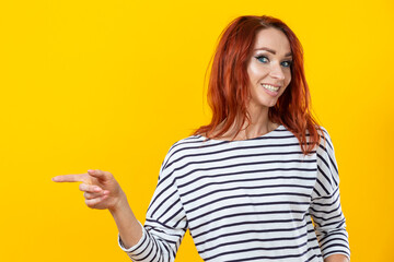 Happy excited cuacaisan winsome ginger girl in striped shirt pointing finger on copy space isolated on golden yellow background