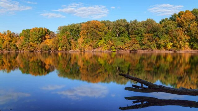 timelapse of beautiful autumn landscape on a bright sunny day, river and forest, blue sky with clouds, sunlight on the yellow leaves of trees and calm water

