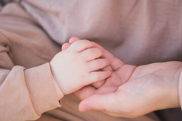 Mom holds the baby's hand in beige clothes.