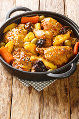Braised chicken meat with spicy sauce, prunes, carrots, potatoes, olives and onions close-up in a frying pan on a wooden table. Vertical