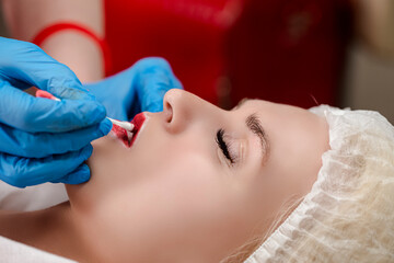 Obraz na płótnie Canvas Young Caucasian Woman During a Process of Permanent Lips Makeup in Tattoo Salon Closeup.