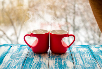 two heart shaped mugs with tea on the background of a window in winter
