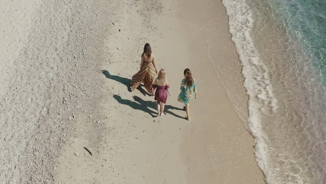 Aerial view of a group of beautiful girls strolling by the sea in the summer morning light in front of a crystal-clear waters in Isca sullo Ionio, Calabria, Italy.