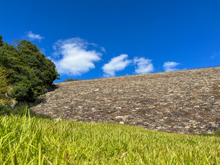 Fototapeta na wymiar 下流の芝生から見上げる黒谷ダムの石積みと青空に連なる雲