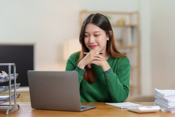 Bright, cute and happy Asian female student study online in the living room using laptop computer in a relaxed manner. Young Asian woman using laptop at home.