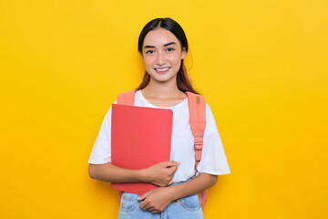 Cheerful pretty young student girl wearing backpack holding books isolated on yellow background