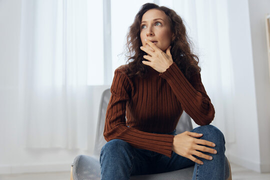 Heavy Thoughts Concept. Frustrated Pensive Thoughtful Curly Adorable Woman Reclines On Hand Lost In Sad Thoughts About Irreparable Mistake Decision About Abortion Sit In Chair At Home Looks Aside