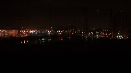 View through side window of railway railroad train that passes bridge over road where cars drive in night city. Lighting from street lamps and lanterns. Travel and tourism concept