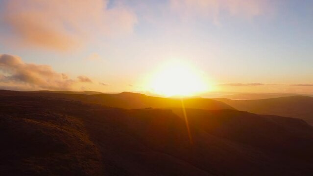 Sunbeam shining behind mountain range during golden sunset - drone shot