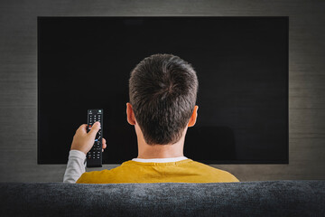 Man watching television, turning on plasma flatscreen TV-set, pointing remote control at empty TV...