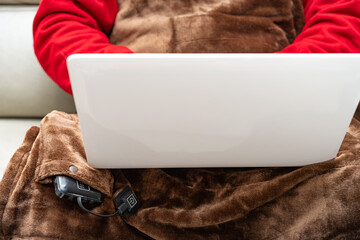 man with an electric blanket and using a laptop on a sofa