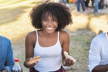 Young woman with afro hair looking at camera and smiling while enjoying having a picnic with friends outdoors in a park.