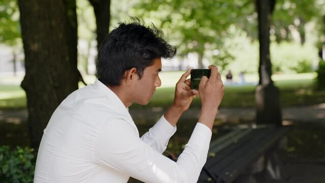 Rear side closeup of Indian man taking pictures of park with smartphone