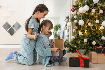 two little girls with presents around the Christmas tree.