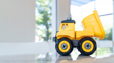 Dump truck, yellow construction toy vehicle with articulated parts built with sturdy plastic is placed on a table.