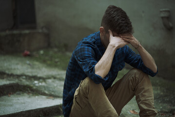 Helpless, hurt, depressed young man feeling completely crushed, sitting outside on a cold day, grieving his fate