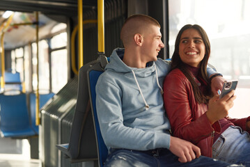 Couple sitting on a bus seat, looking at a phone, hugging and having good times browsing the internet while commuting