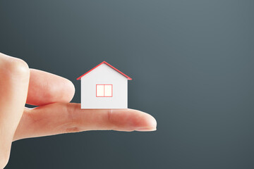 Fototapeta na wymiar Real estate concept with small white and red house layout on human finger on dark background