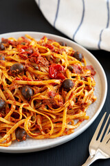 Homemade Tuna Linguine Pasta with Tomatoes, Olives and Capers on a Plate on a black background, side view.