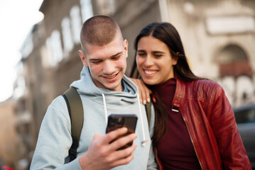 Cute young couple walking the streets of city, looking at a phone together