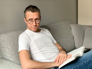 Middle aged man is spending holiday at home. Looking bored of streaming tv and reading book. 