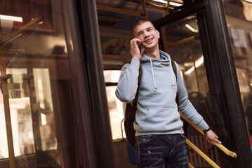 Teenage man getting off the bus and talking on his phone, finished school and exiting on a bus stop