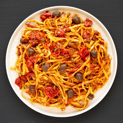 Homemade Tuna Linguine Pasta with Tomatoes, Olives and Capers on a Plate on a black background, top view. Overhead, from above, flat lay.