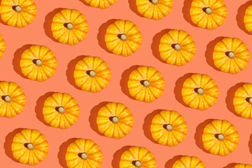 A hard light pattern of a small yellow decorative pumpkin on a bright orange seamless background, top view