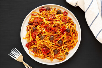 Homemade Tuna Linguine Pasta with Tomatoes, Olives and Capers on a Plate on a black background, top view. Overhead, from above, flat lay.