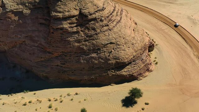 Aerial view of a car driving on a dirt road in front of large mountains in Al Ula, Saudi Arabia - circling, drone shot