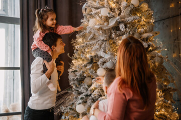  family mother, father, brother and sister are decorating a Christmas tree.