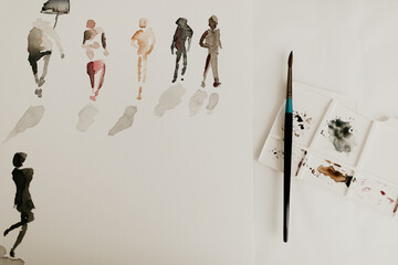 Painted people silhouette on white paper and a mixing palette with paint brush. Flat lay, top view copy space. A variety of people and color, diverse characters. 