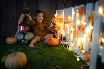 

Cute small baby is staying near a lot of pumpkins in at autumn and halloween decorated scenography. Studio photography.