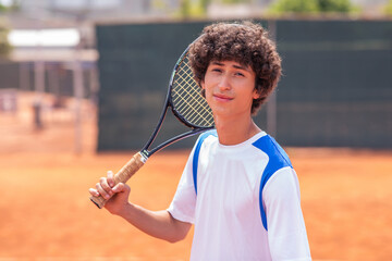 Concept of professional sport charismatic handsome tennis player guy posing in front of the camera he smiling and holding the racket on hands and wearing the uniform